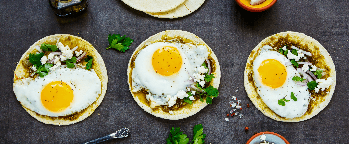 tortillas with fried egg garnished with cilantro & crumbled cheese placed on a rustic background
